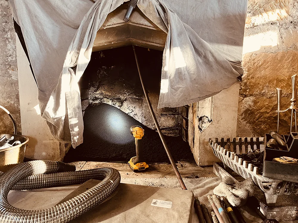 Chimney sweep cleaning an open fire with dust sheets and vacuum equipment near Stirling